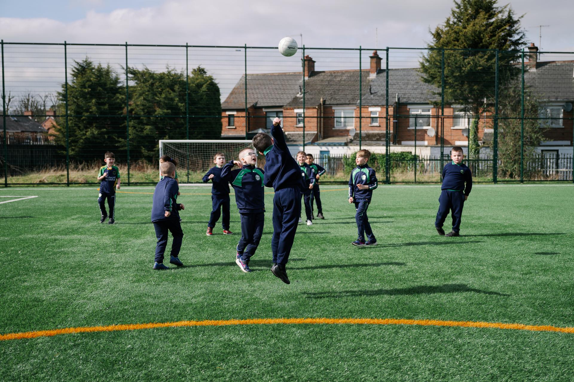 Paisti ag sugradh peil agus ag rith thart ar scoil. / Children play football and running about at school.
